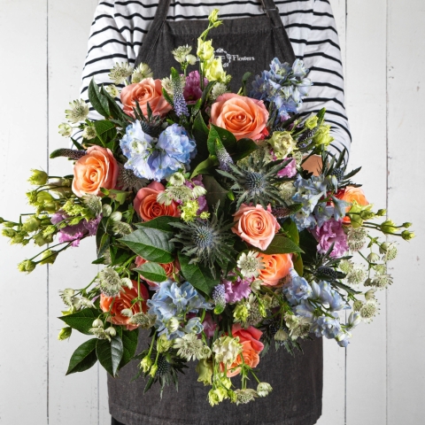 Summer Soiree Bouquet featuring peach roses, blue delphiniums, and seasonal blooms