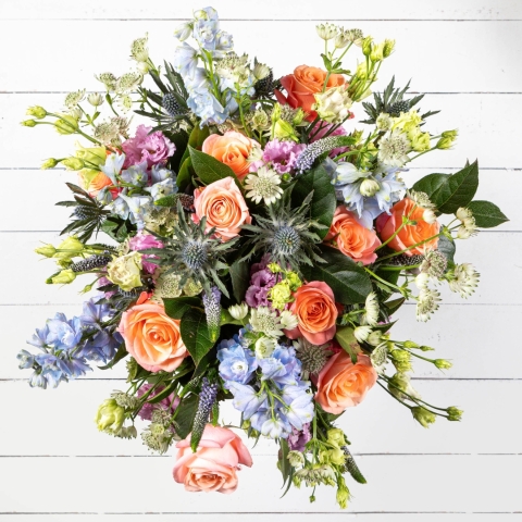 Summer Soiree Bouquet featuring peach roses, blue delphiniums, and seasonal blooms